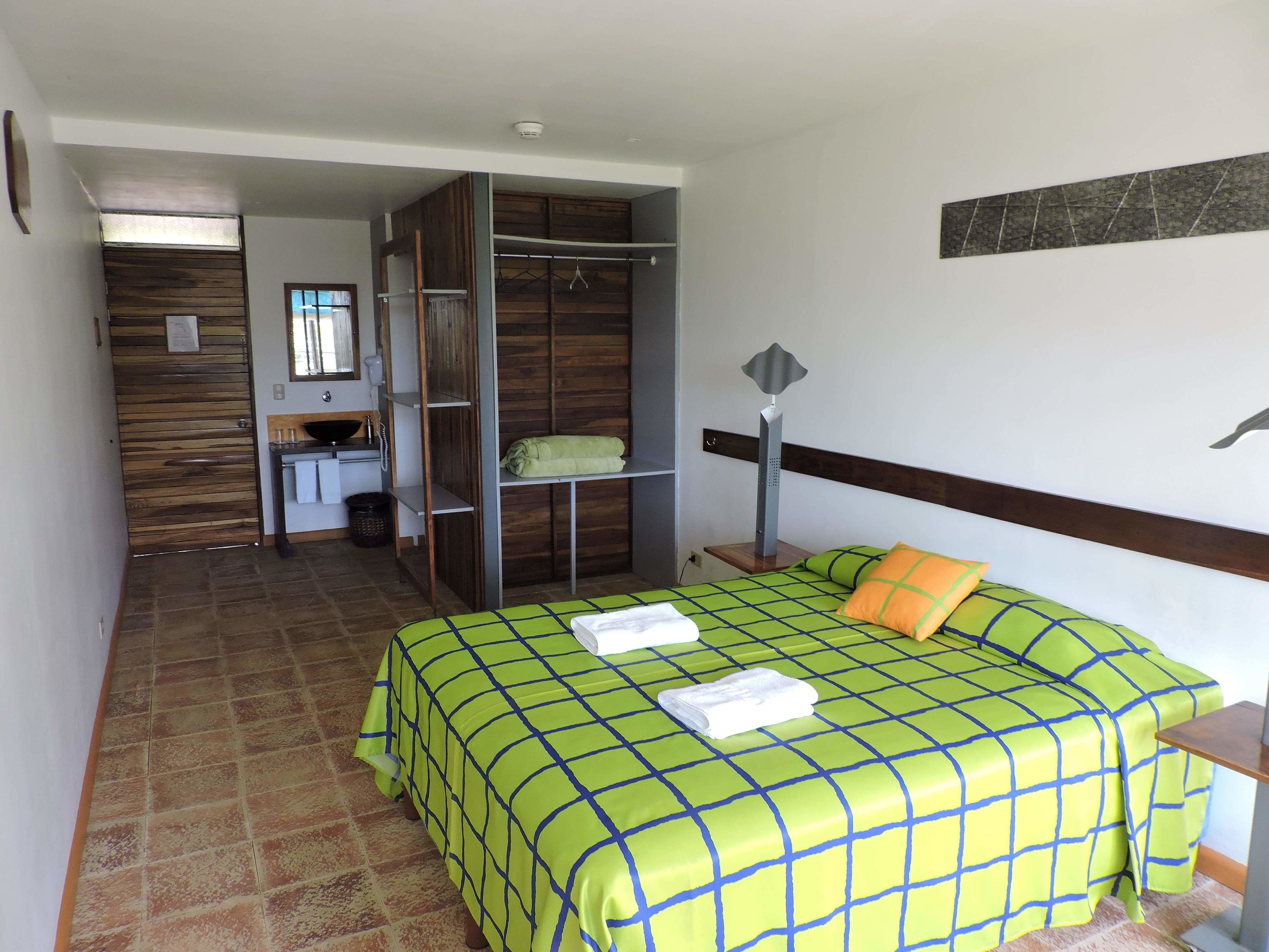 A bedroom with a bed, a nightstand, a bedside table, a wardrobe, a mirror, and a bathroom with a sink and a toilet.