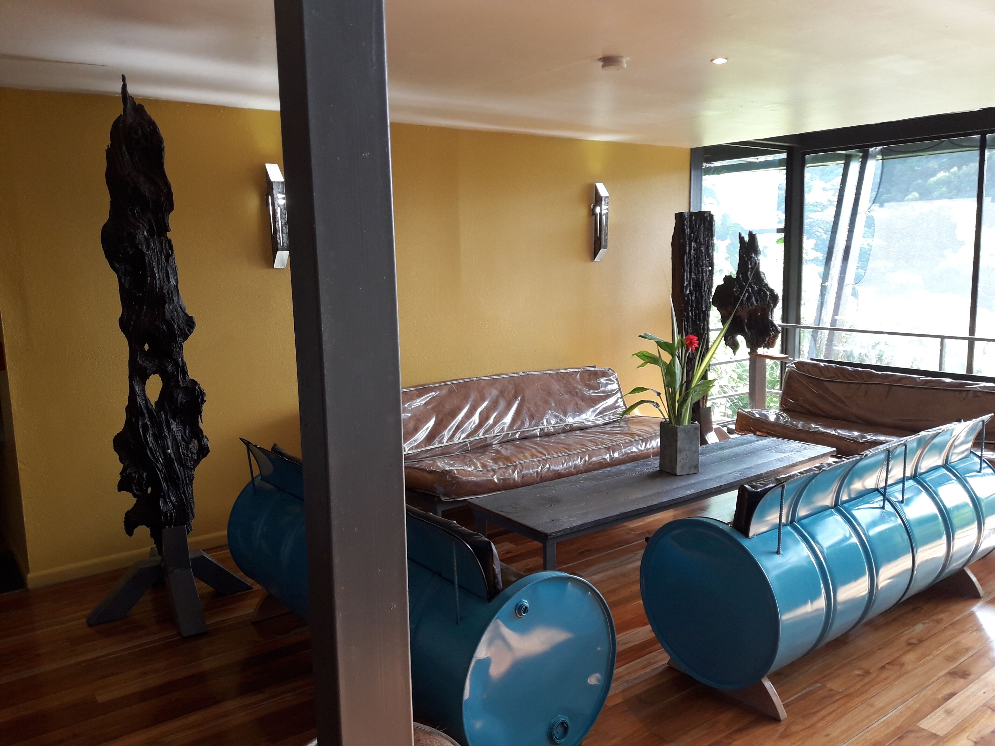 A modern living room with a brown leather sofa, a glass coffee table, and blue barrel-shaped stools.