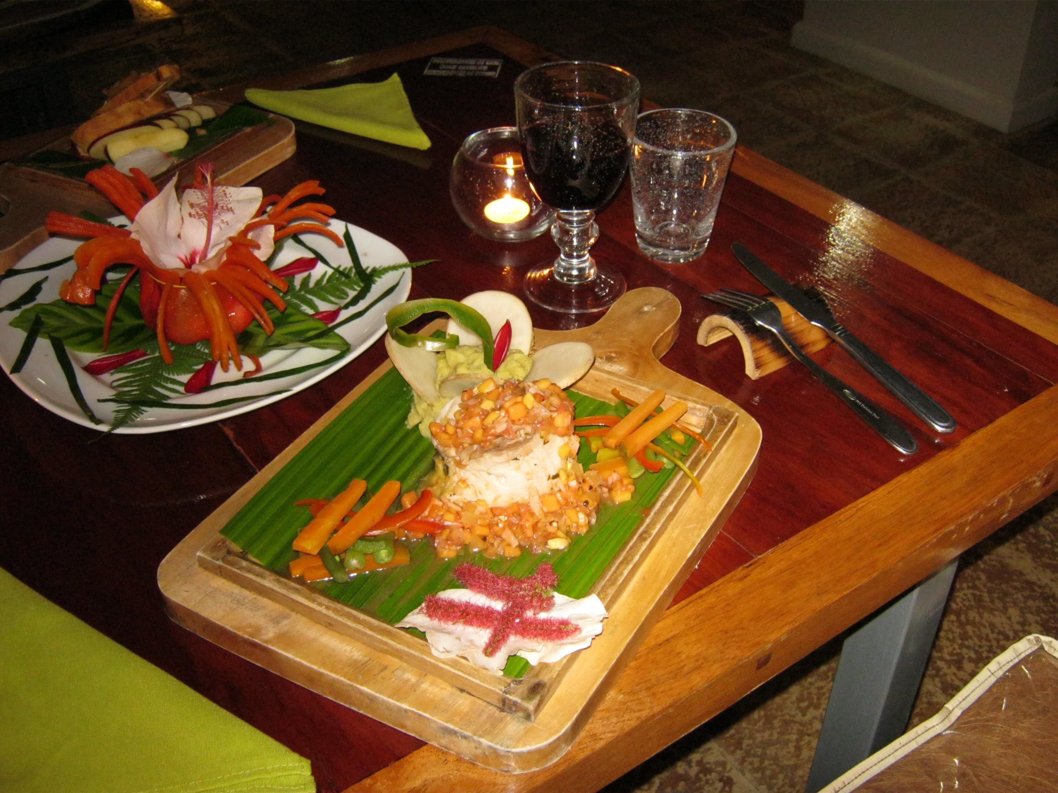 A dining table with a variety of dishes, including a plate with a fish dish, a plate with a vegetable dish, and a glass of red wine.
