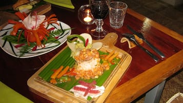A dining table with a variety of dishes, including a plate with a fish dish, a plate with a vegetable dish, and a glass of red wine.