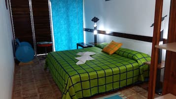 Un dormitorio con una colcha verde a cuadros, una cortina azul, un cabecero de madera, una mesita de noche y una silla azul.