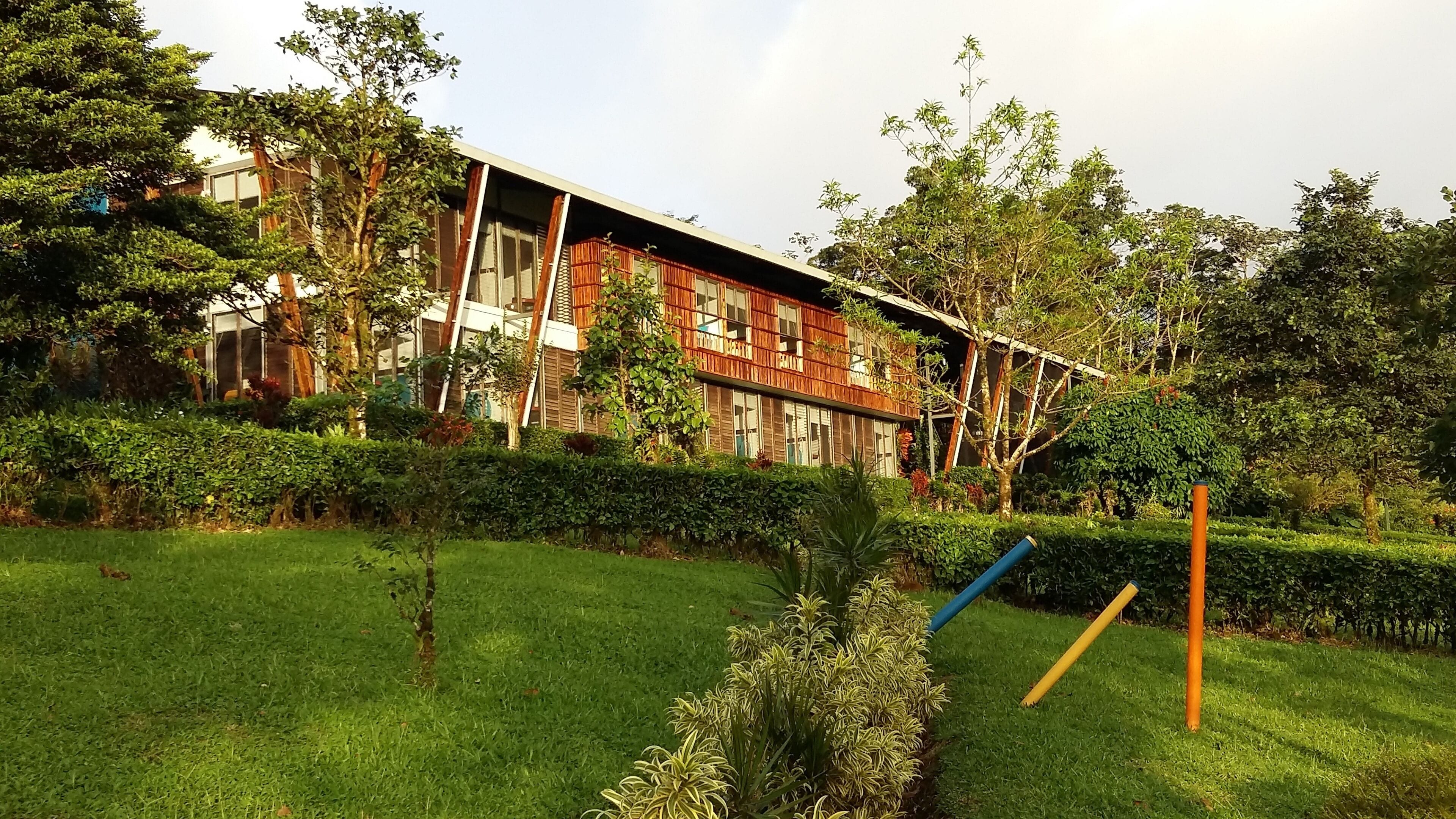 A modern building with a wooden facade and large windows, surrounded by well-maintained greenery and a grassy lawn.
