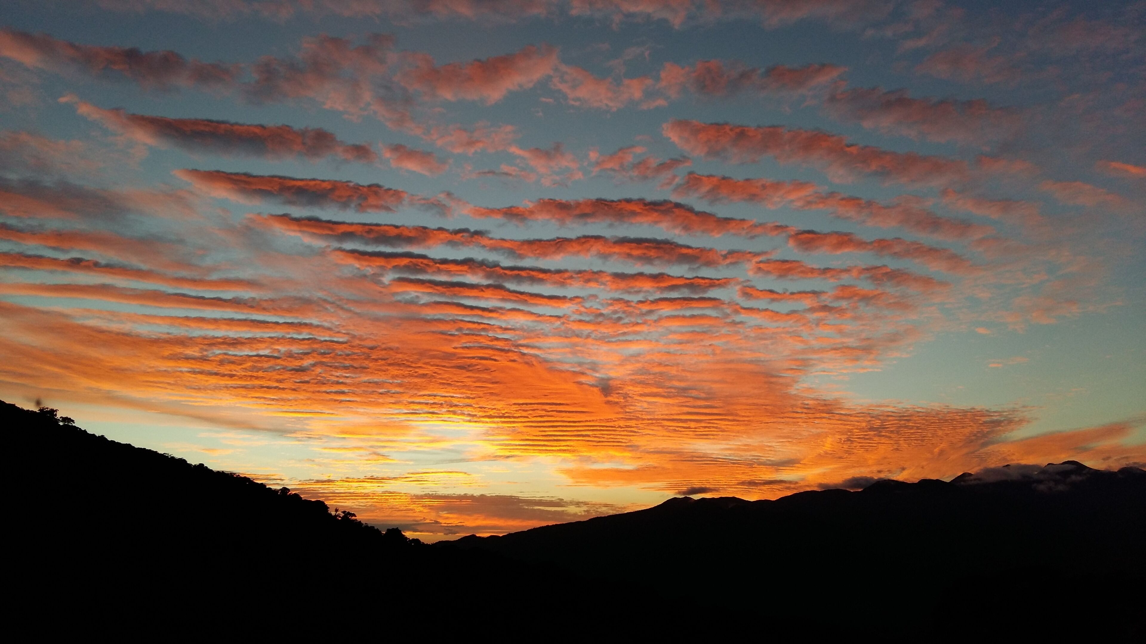 Um pôr do sol com formação de nuvens sobre uma cordilheira.