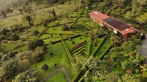 A large, modern building with a red roof, surrounded by well-manicured gardens and a hilly landscape. - Celeste Mountain Lodge (Bijagua)