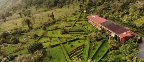 A large, modern building with a red roof, surrounded by well-manicured gardens and a hilly landscape.