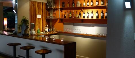 A bar area with a wooden counter, bar stools, and shelves of bottles and glasses.