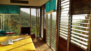 A room with a bed, a small table, and a view of greenery through the window. - Celeste Mountain Lodge (Bijagua)