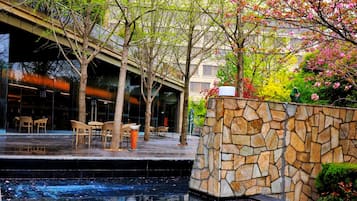 An outdoor seating area with tables and chairs, a stone wall, and a water feature.