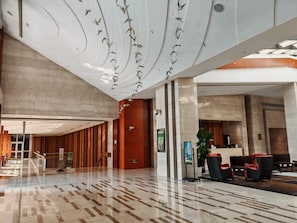Een ruime lobby met een modern design, met een receptiebalie, zithoek en een trap.