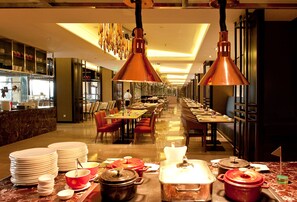 A hotel dining area with multiple tables and chairs, a buffet setup with plates and bowls, and hanging copper pendant lights. - Crowne Plaza Shanghai Anting by IHG (Shanghai)