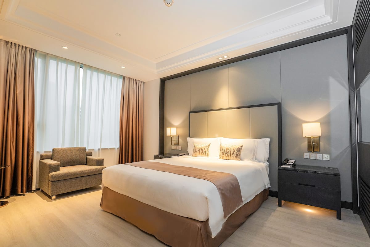 Habitació d'hotel moderna amb un llit gran, zona de seients i una nitzeta amb una làmpada.