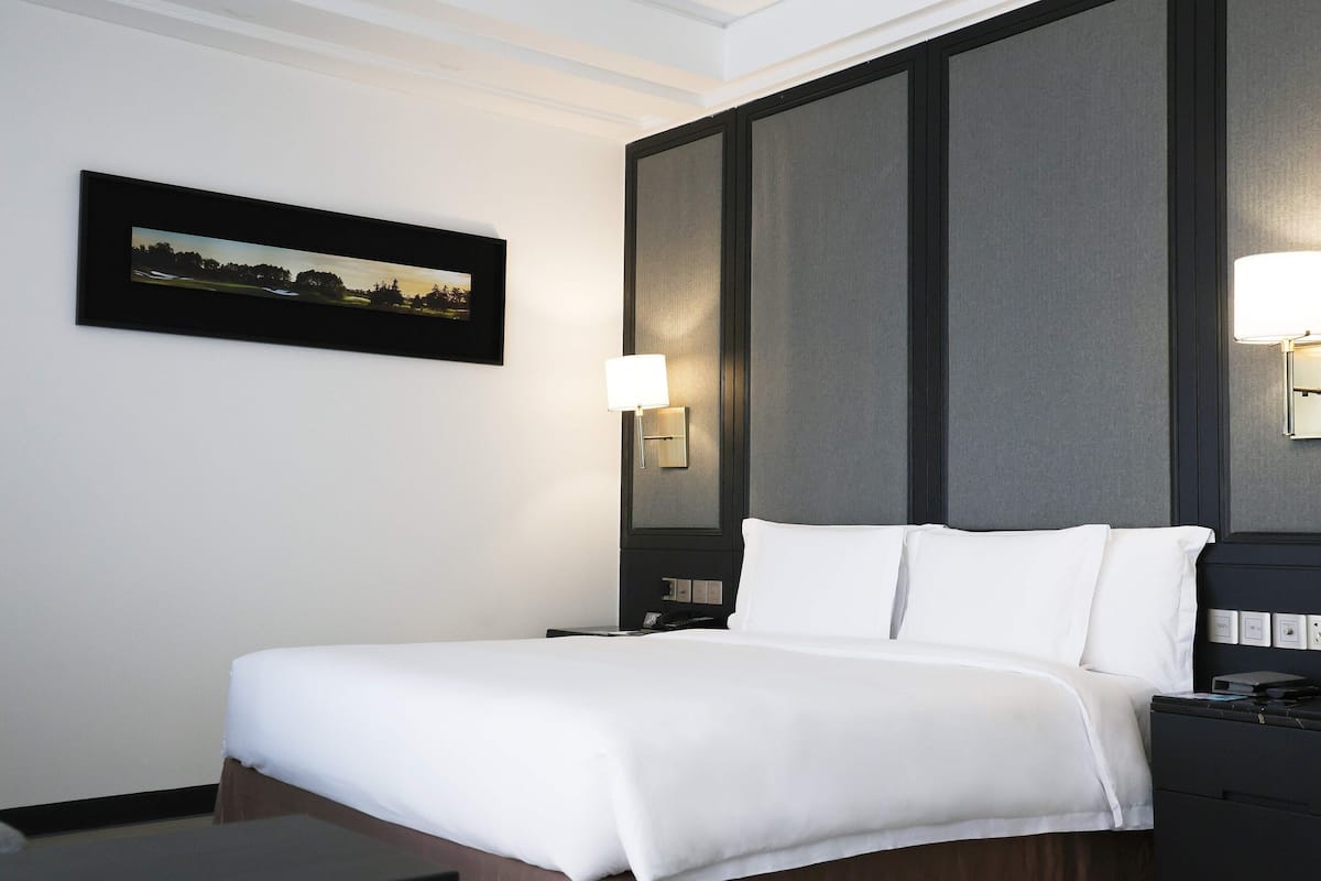 A neatly made bed with white linens, a bedside table with a lamp, and a framed picture on the wall.