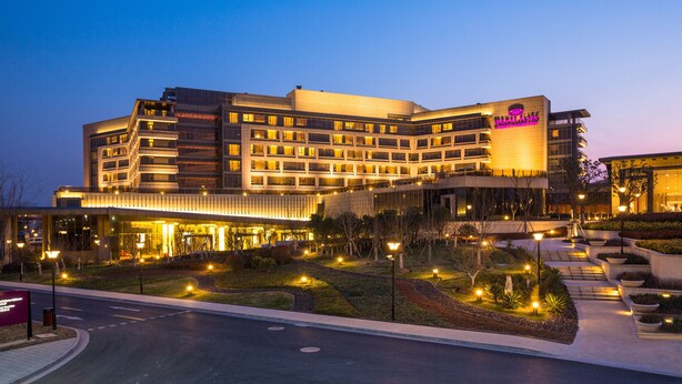 Un hotel de varios pisos con un diseño arquitectónico moderno, que cuenta con una entrada destacada y zonas exteriores bien iluminadas.