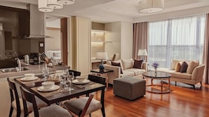 Una habitación de hotel moderna con zona de comedor, sofá y un ventanal con cortinas.