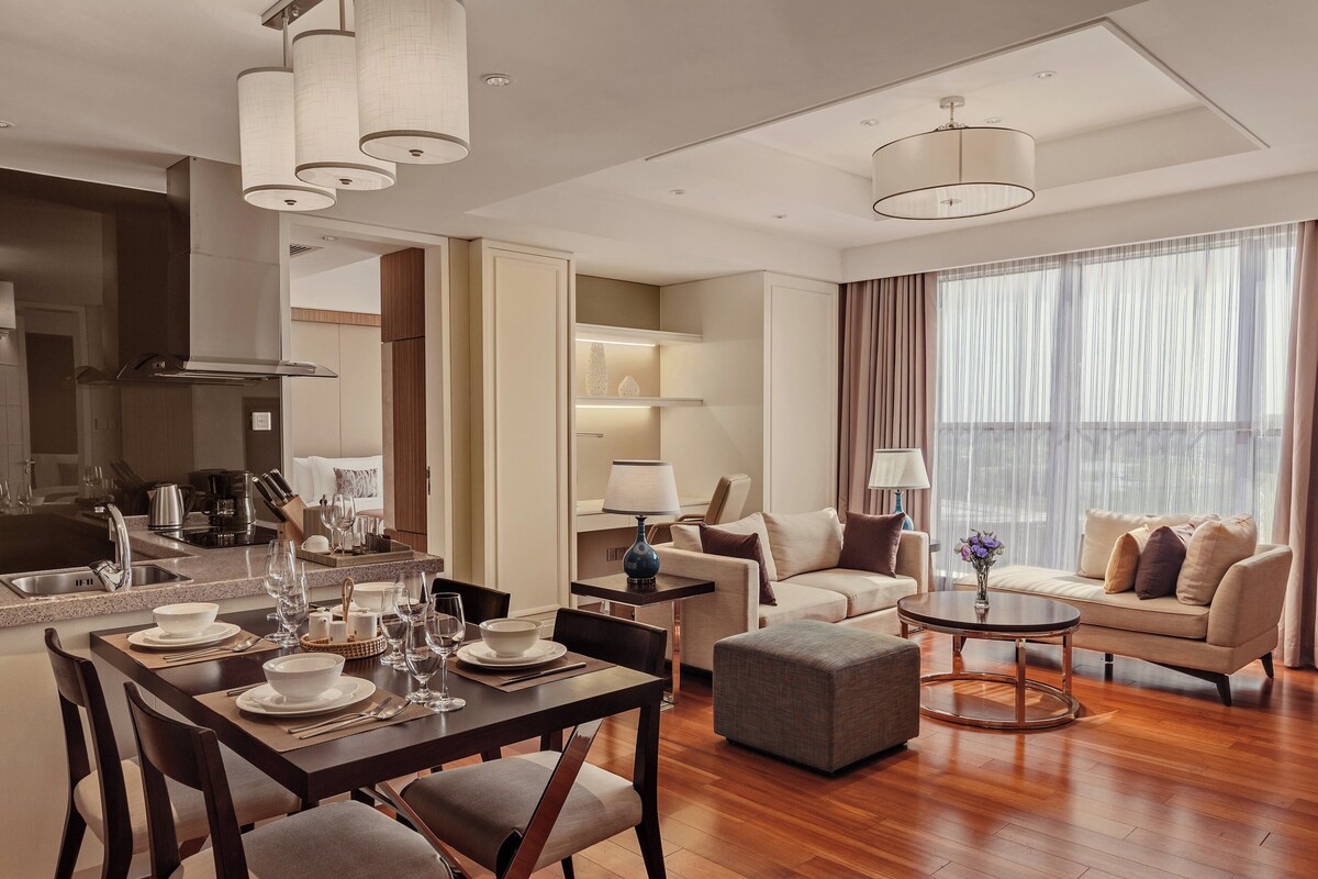 A modern living room with a dining area, a sofa set, and a kitchen in the background.