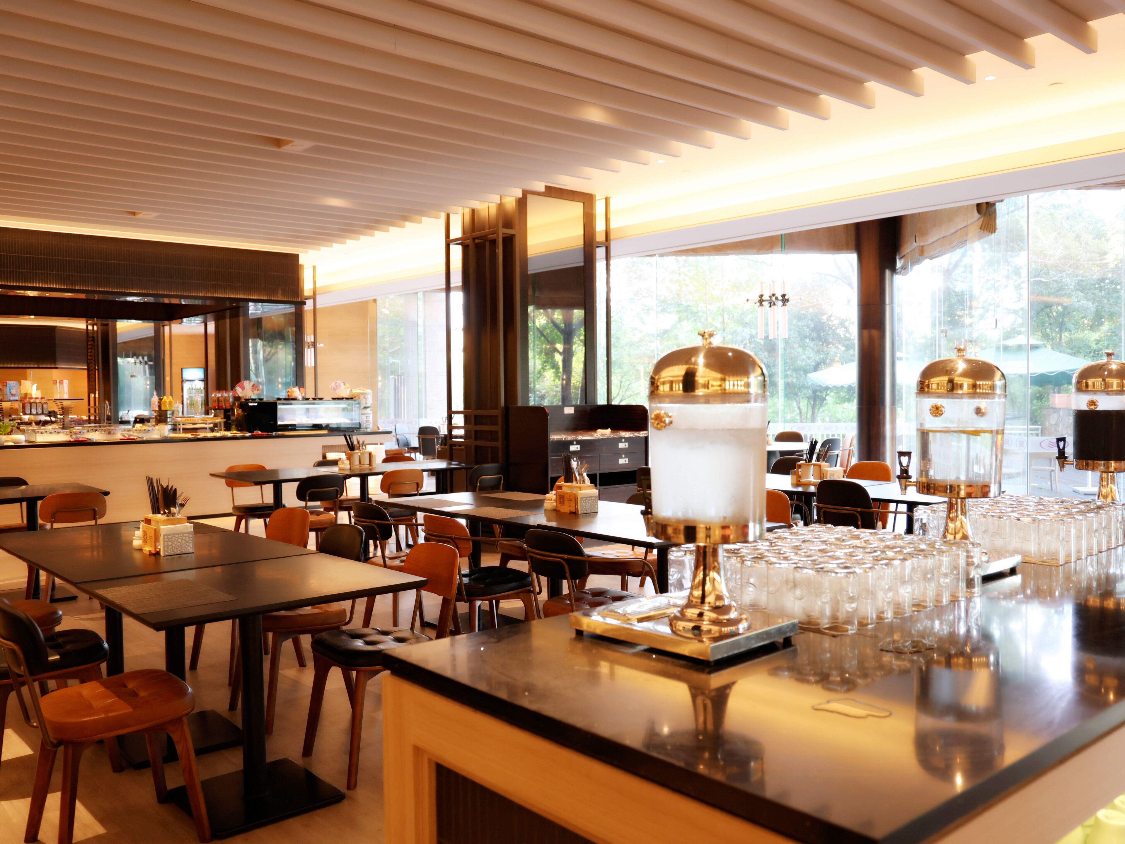 A modern restaurant interior with multiple dining tables, chairs, and a bar area.