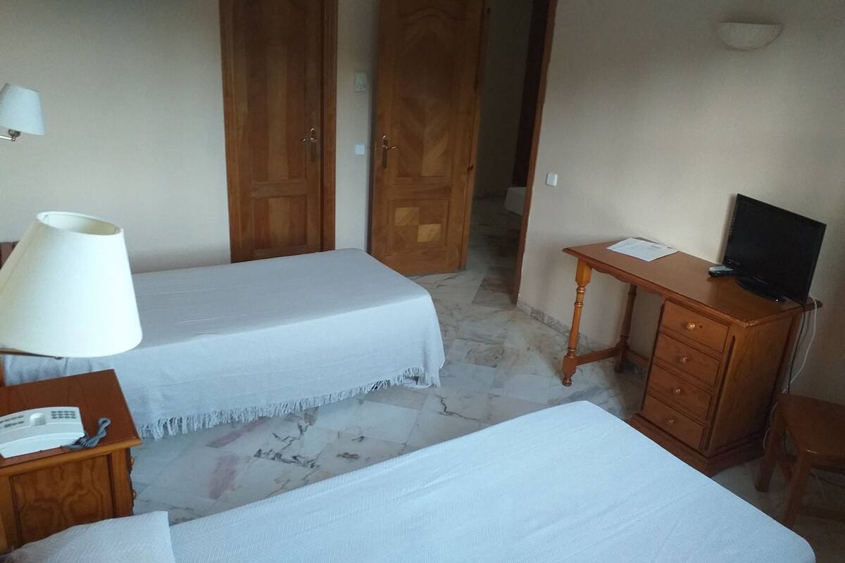 A hotel room with two beds, a desk with a television, a lamp, and a telephone.