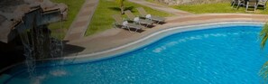 A swimming pool with a waterfall feature, surrounded by a grassy area and lounge chairs.