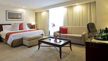 A hotel room with a bed, a sofa, a coffee table, and a desk.