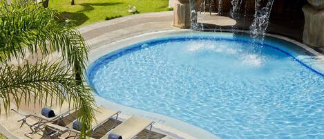 A swimming pool with a waterfall feature, surrounded by lounge chairs and palm trees.