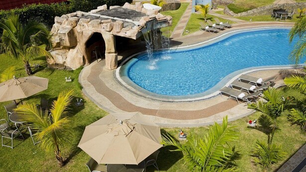 A swimming pool with a waterfall feature, surrounded by lounge chairs and umbrellas. - Eurobuilding Express Barinas (Barinas)