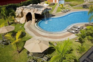 Piscina com cachoeira, rodeada por espreguiçadeiras e guarda-sóis.