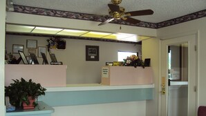 A reception area with a desk, framed certificates, a clock, and a ceiling fan. - Western Motel (Folkston)