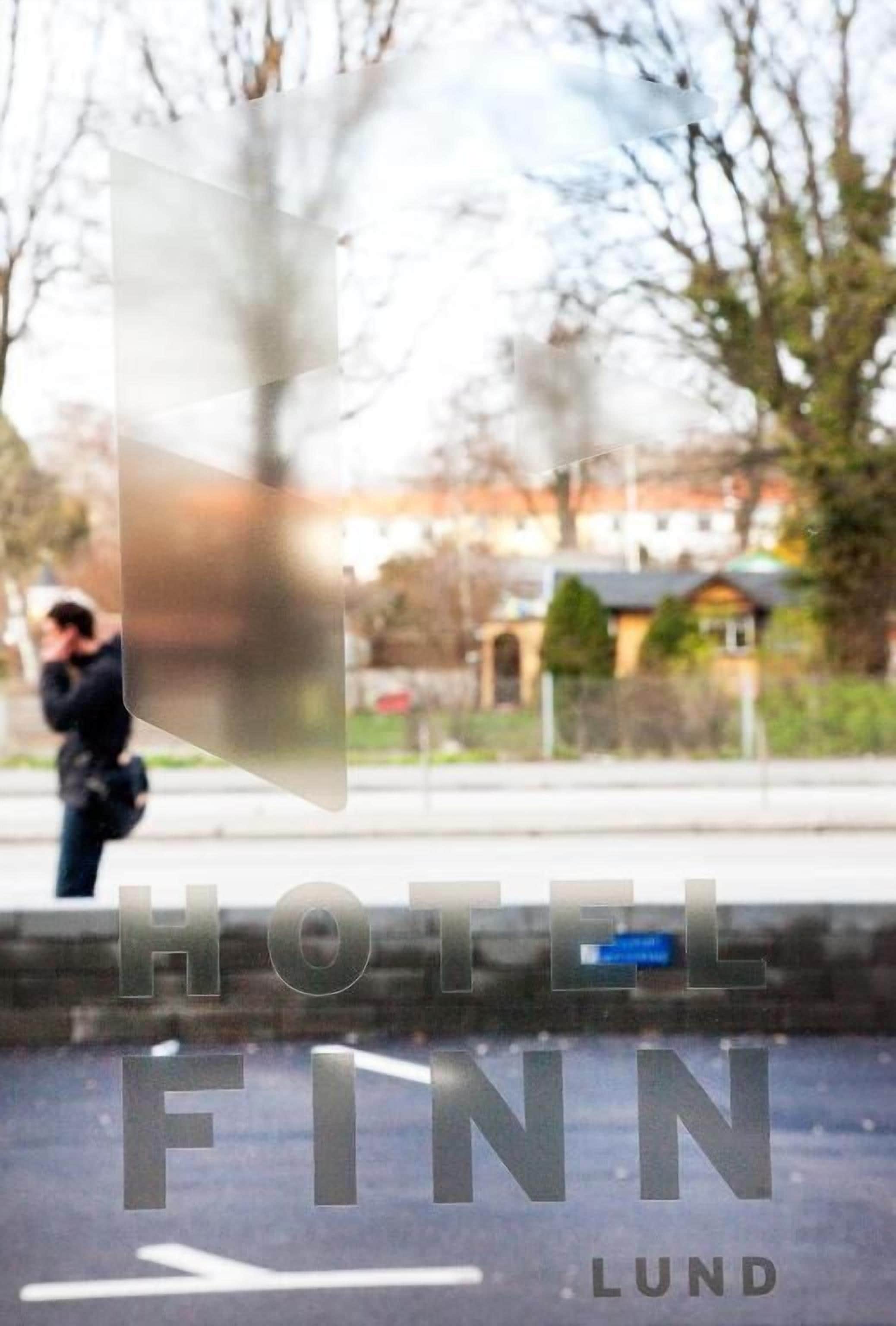A blurred view of a person walking past a building with the text "HOTEL FINN LUND" visible.
