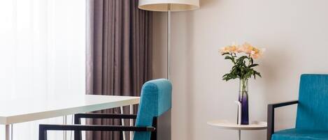 Una habitación de hotel con una silla azul, una mesa blanca, una lámpara de pie y un florero con flores.
