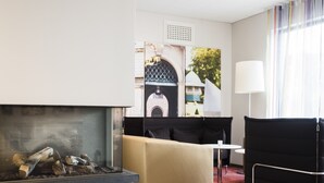 Una habitación de hotel moderna con chimenea, un sofá, una mesita y vistas a un edificio a través de una ventana.