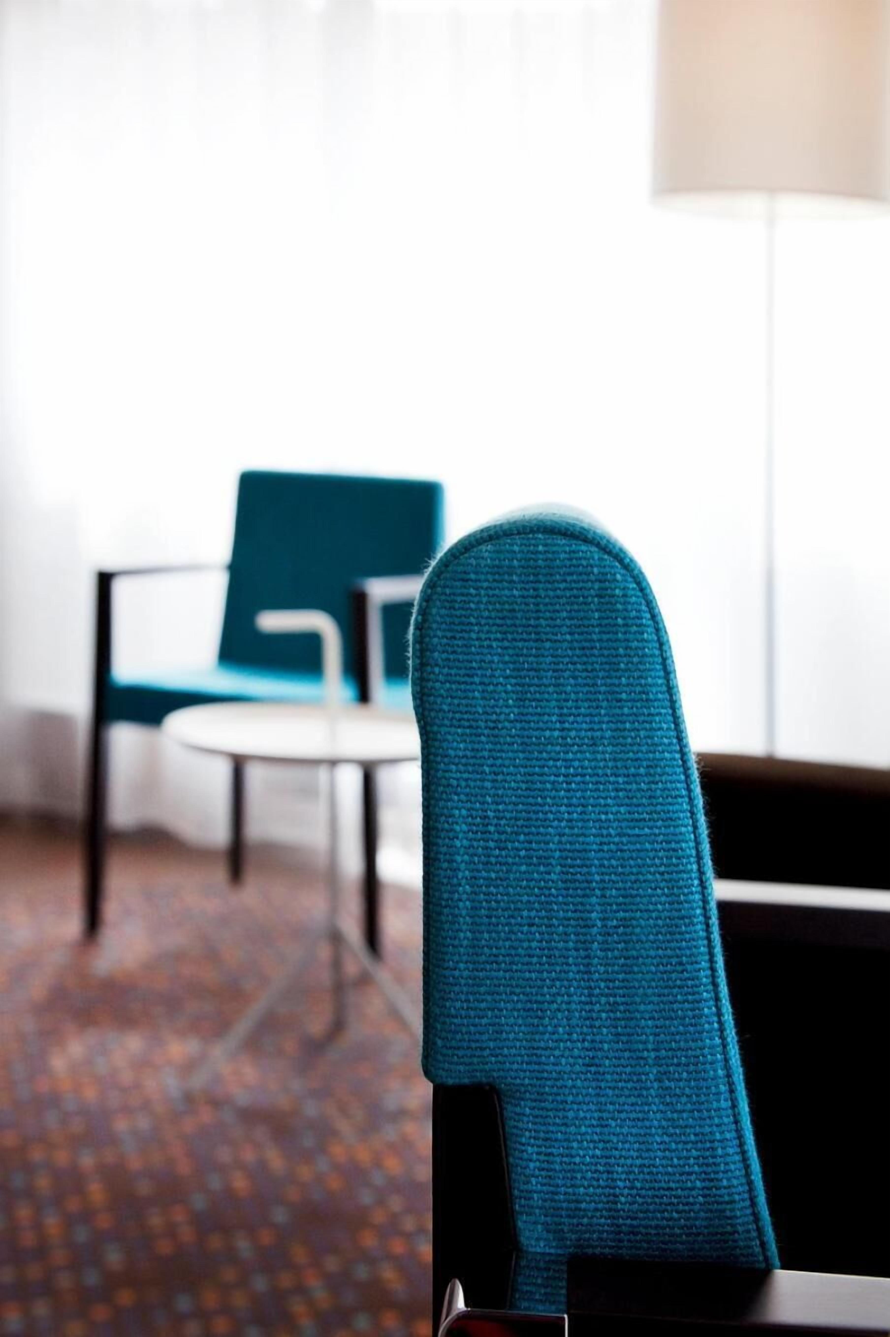 A room with a teal chair, a round table, and a lamp.