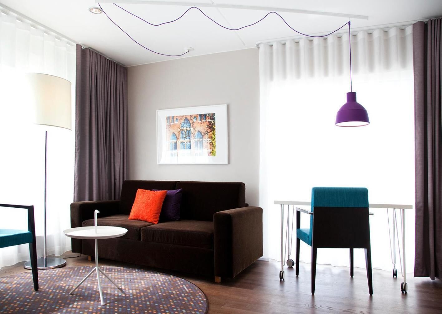 A modern living room with a sofa, a round coffee table, a blue armchair, and a purple pendant light.