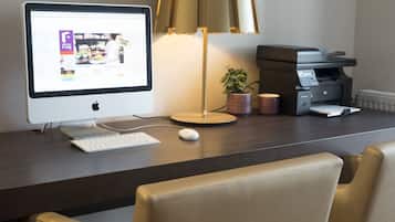 Escritorio de habitación de hotel con una computadora de escritorio, una lámpara, una impresora y una planta en maceta.