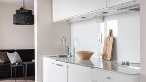 Una cocina moderna con armarios blancos, encimera de vidrio, pileta de acero inoxidable y lámpara colgante.