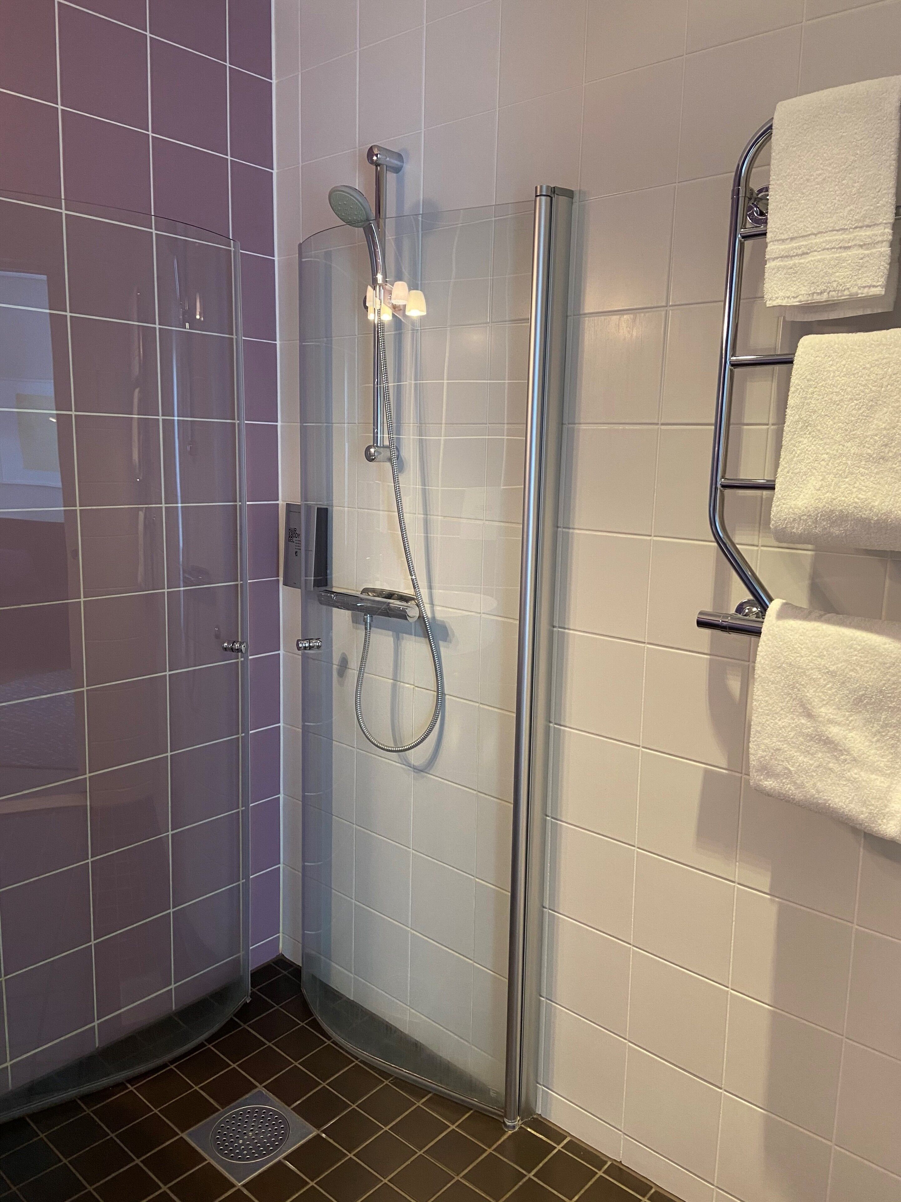 Une salle de bain moderne dotée d’une douche à parois de verre, d’un porte-serviettes avec plusieurs serviettes et d’un sol carrelé.