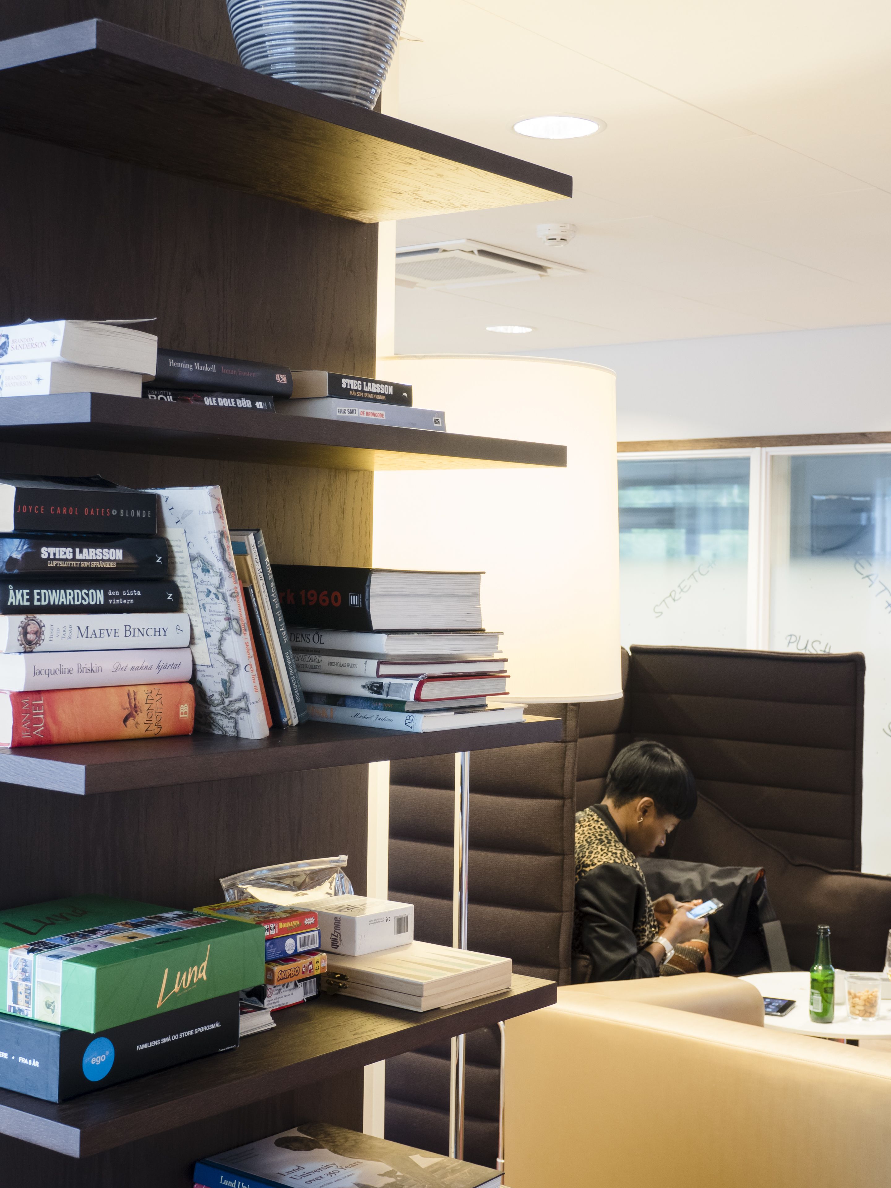 A modern office space with a bookshelf filled with books, a desk with a laptop, and a comfortable seating area.