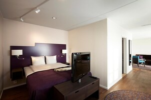 Moderni hotellihuone, jossa on suuri sänky, taulutelevisio ja työpöytä tuolilla.