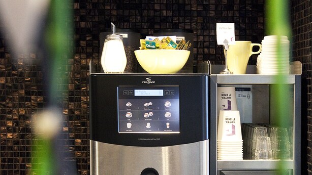 Un dispensador de agua con grifo para agua caliente, una cafetera y un refrigerador.