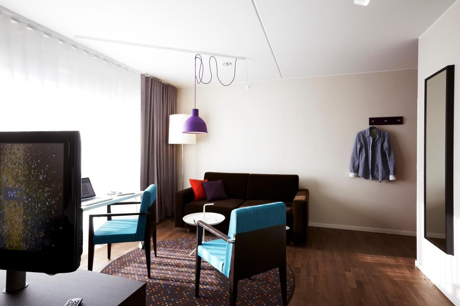 Una habitación de hotel moderna con sofá, sillas, escritorio y televisor.