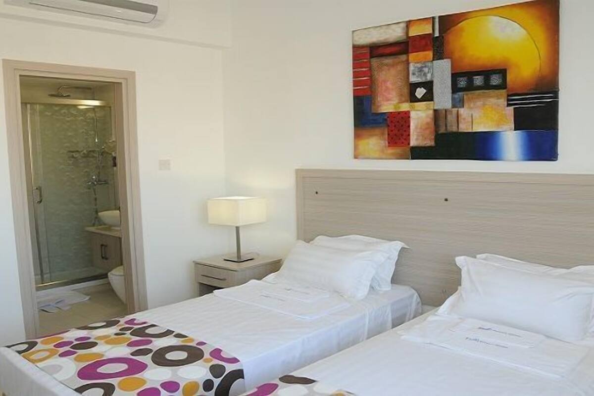 Quarto de hotel com duas camas, banheiro e um quadro na parede.