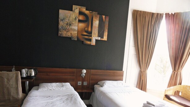 A hotel room with two single beds, a wooden headboard, a wall-mounted artwork, a bedside table with a lamp, and a window with curtains. - Blossom Guest House (Edinburgh)