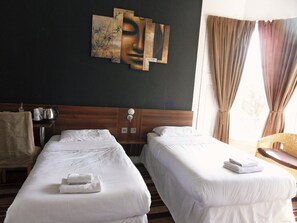 A hotel room with two single beds, a wooden headboard, a wall-mounted artwork, a bedside table with a lamp, and a window with curtains. - Blossom Guest House (Edinburgh)