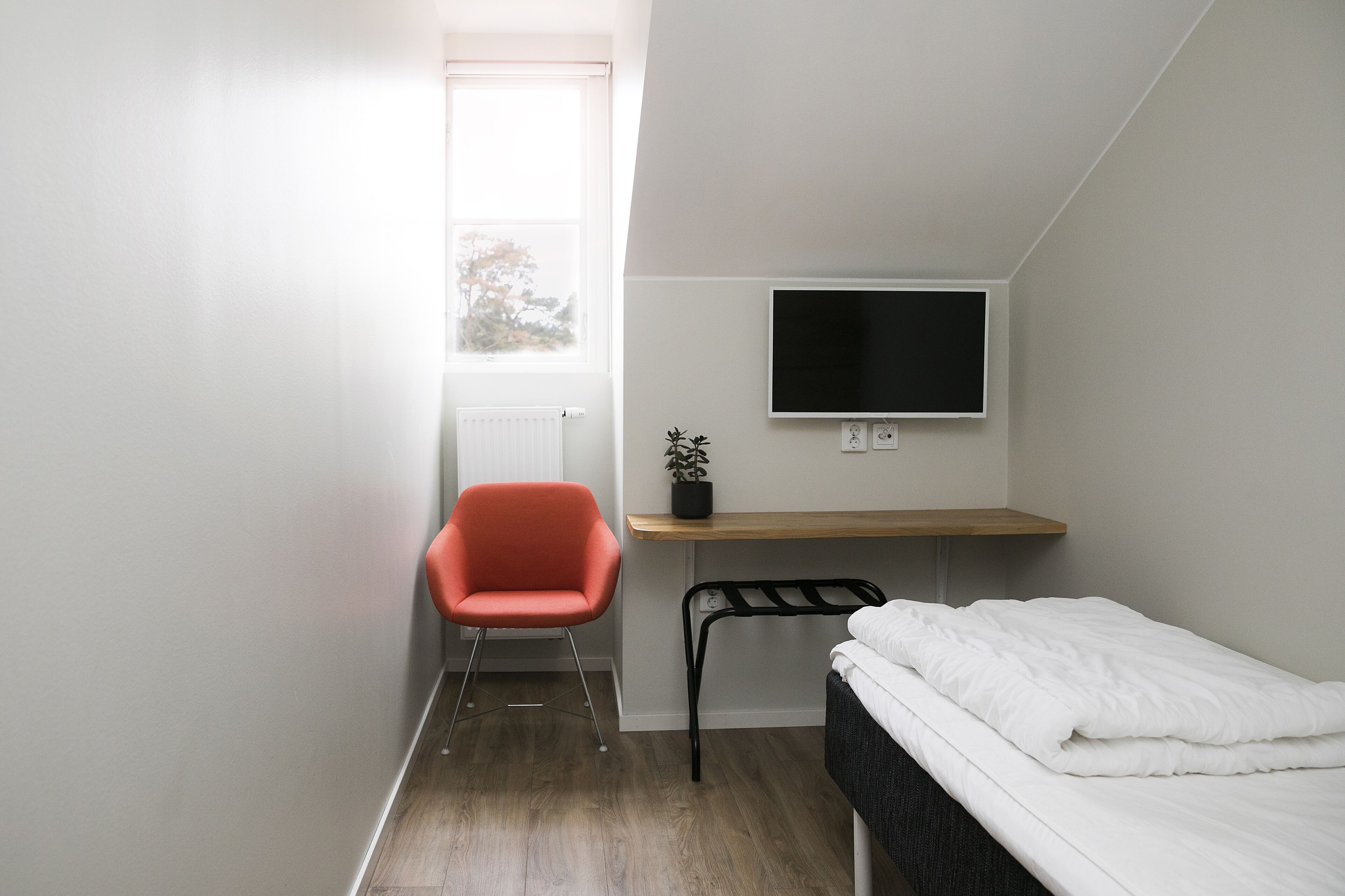 A small, modern room with a bed, a desk with a TV, a chair, and a window.