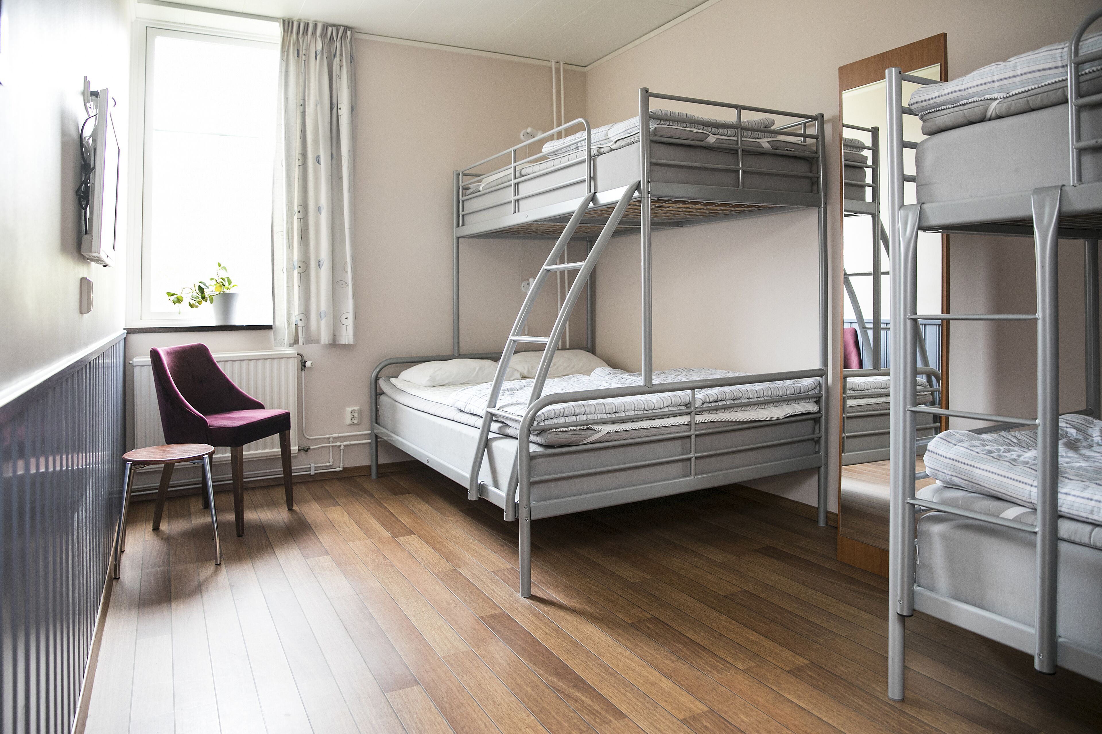 Ein Schlafsaalzimmer mit Etagenbetten, einem Stuhl, einem Heizkörper und einem Fenster mit Vorhängen.