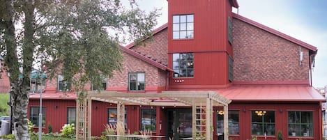 A red brick building with a covered patio area, large windows, and a small garden.