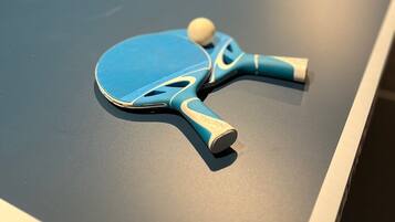 A table tennis table with a blue table and net, and a blue paddle with a ball on it.