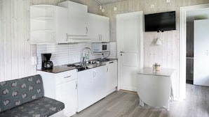 A compact kitchen with white cabinets, a microwave, and a coffee maker. There is a small white table and a sofa with a patterned cushion. - Kvibergs Vandrarhem - Hostel (Gothenburg)