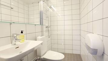A modern bathroom with white tiles, a glass shower enclosure, a sink with a soap dispenser, and a toilet.