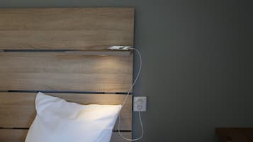 A bed with a wooden headboard, a white pillow, and a power outlet on the wall.