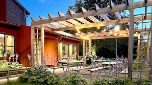 A covered patio area with wooden tables and benches, surrounded by lush greenery and flowering plants. - Kvibergs Vandrarhem - Hostel (Gothenburg)